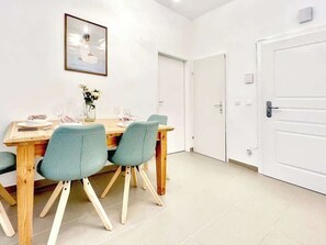 A dining area with a wooden table and four chairs, a vase with flowers, and a framed picture on the wall. - Servus Homes - Metro Stadthalle - FRANZ (Wien)