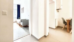 Ein Hotelzimmer mit einem Bett, einem Schreibtisch und einem Stuhl. Es gibt ein Fenster mit Vorhängen, eine Heizung und einen Lichtschalter an der Wand.