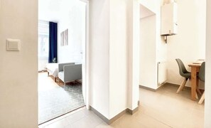 Ein Hotelzimmer mit einem Bett, einem Schreibtisch und einem Stuhl. Es gibt ein Fenster mit Vorhängen, eine Heizung und einen Lichtschalter an der Wand.