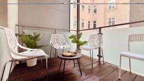 A balcony with a wooden floor, white metal chairs, and potted plants. - Servus Homes - rooftop terrace & balcony - Metro (Wien)