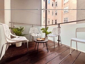 Ein Balkon mit Holzboden, weißen Metallstühlen und Blumentöpfen.