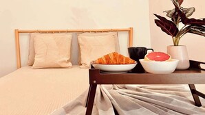 A neatly made bed with a headboard, a table with a bowl of food, a cup, and a plant. - Servus Homes - rooftop terrace & balcony - Metro (Wien)