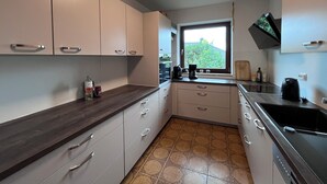A kitchen with white cabinets, a dark countertop, a window with a view, and a stove. - Mühlenberg Vacation Home (Grebin)