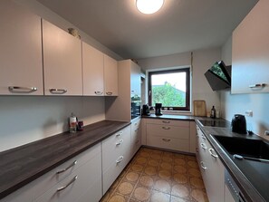 Eine Küche mit weißen Schränken, einer dunklen Arbeitsplatte, einem Fenster mit Blick und einem Herd.