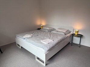 A single bed with a white frame, two bedside tables with lamps, and a grey carpeted floor. - Mühlenberg Vacation Home (Grebin)