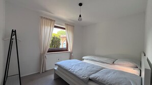 A small, single-bed room with a window, a hanging light fixture, and a black metal stand. - Mühlenberg Vacation Home (Grebin)