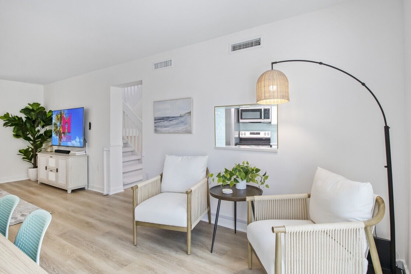 Un salon moderne avec un téléviseur, un coin salon et une cuisine visible à travers une fenêtre.