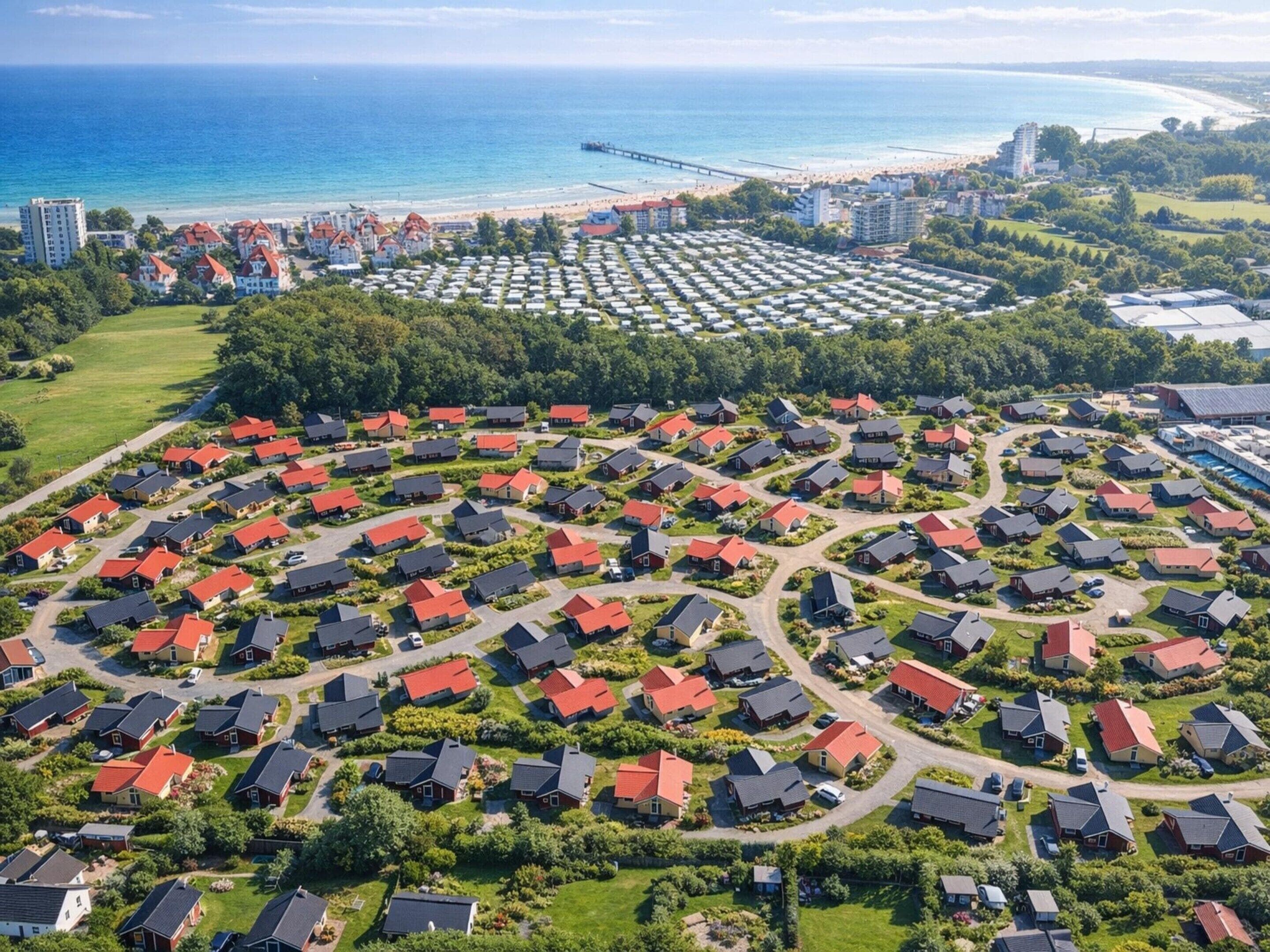 An aerial view of a residential area with houses arranged in a circular pattern, surrounded by greenery, with a beach and ocean in the background.