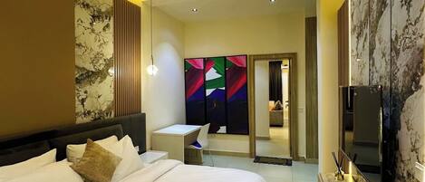 A modern hotel room with a large bed, a desk, a TV, and a bathroom visible through a glass door.