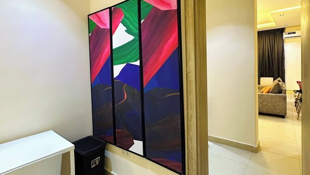 A room with a white desk, a black trash bin, and a colorful abstract painting on the wall.
