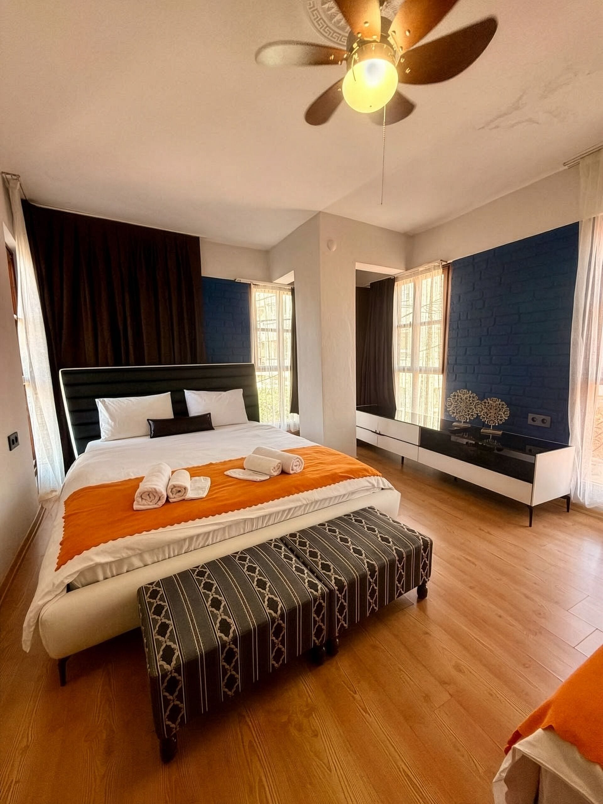 Habitación de hotel con cama, reposabajares y ventilador de techo, ofreciendo vista al exterior.