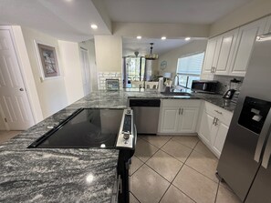 A modern kitchen with a granite countertop, built-in dishwasher, white cabinets, and a stainless steel refrigerator. - Sunny 2BR Condo w/ Heated Pool — Minutes to IMG Academy & Beaches (Bradenton)