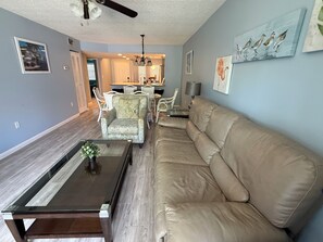 A modern living room with a leather sofa, a glass coffee table, and a dining area with white chairs. - Cozy 2-bedroom condo in peaceful Bradenton ground floor (Bradenton)