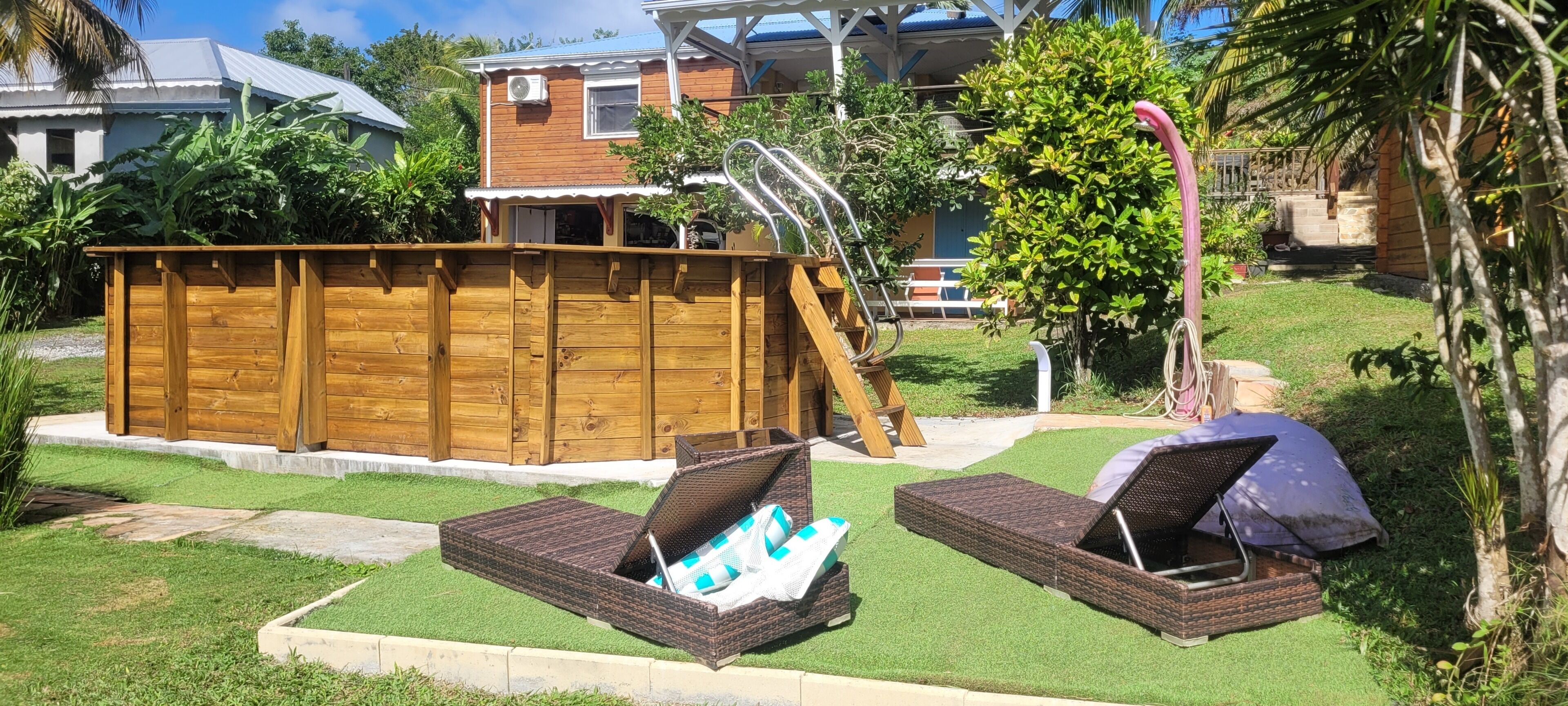 Een achtertuin met een houten terras, een klein zwembad en twee rieten lounge fauteuils.