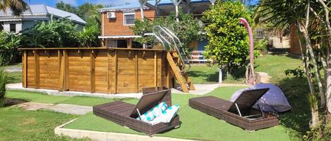 Un jardin avec une terrasse en bois, une petite piscine et deux fauteuils de jardin en osier.