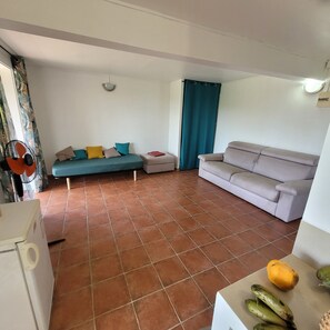 Ein Wohnzimmer mit einer Couch, einem kleinen Sofa, einem Tisch mit Früchten und einem Ventilator.