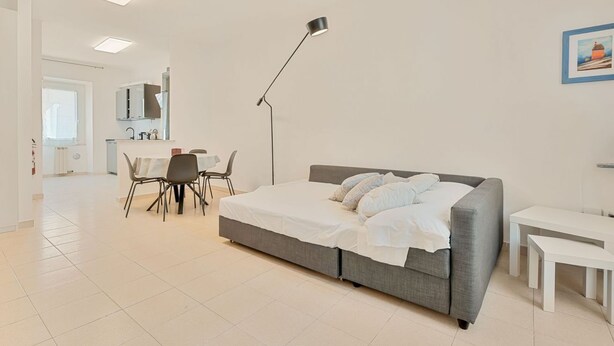 Een moderne slaapkamer met een grijs bed, witte beddengoed, een bureau en een stoel.
