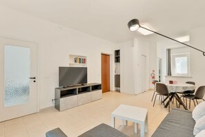 Ein modernes Wohnzimmer mit Fernseher, Essbereich mit Tisch und Stühlen sowie einer Couch.