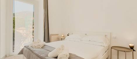 A bedroom with a large bed, a bedside table, a nightstand, a window with a view, and a chandelier.