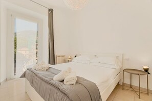 A bedroom with a large bed, a bedside table, a nightstand, a window with a view, and a chandelier. - [AMA] Holiday home-5Terre-Near the station (La Spezia)