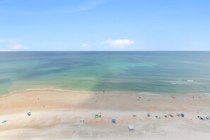 Ein Strand mit klarem Wasser, sandigem Ufer und mehreren Sonnenschirmen.
