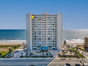 Ein mehrstöckiges Hotel mit auffälligem Sternenlogo, einem Parkplatz und Blick auf den Strand.