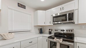 A kitchen with white cabinetry, a built-in microwave, a stove, and a window with blinds. - Castle Reef 527 (New Smyrna Beach)