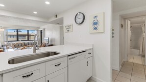 A modern kitchen with a large island, white cabinetry, and a wall-mounted clock. - Castle Reef 527 (New Smyrna Beach)