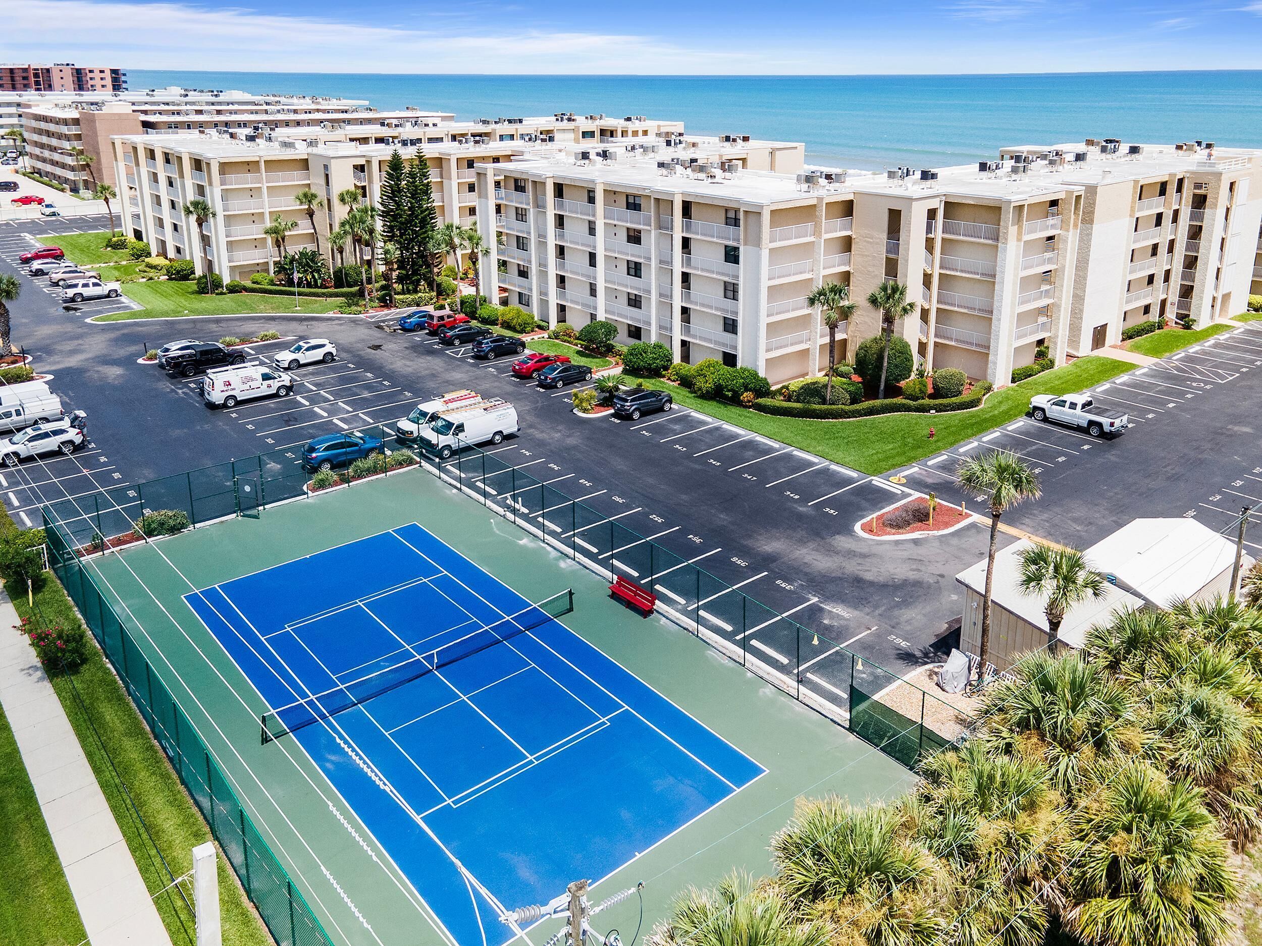 Un hotel de varios pisos con cancha de tenis, estacionamiento y vista al océano.