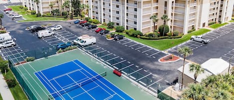 Un hotel de varios pisos con cancha de tenis, estacionamiento y vista al océano.
