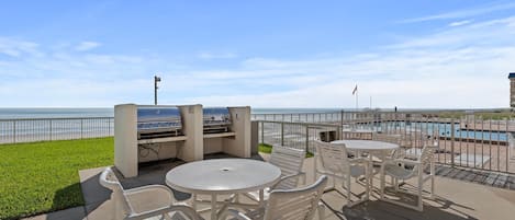 Un patio exterior con piscina, estaciones de parrillada y sillas blancas.