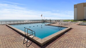 A rectangular swimming pool with a white deck, a flag, and a view of the beach. - Castle Reef 527 (New Smyrna Beach)