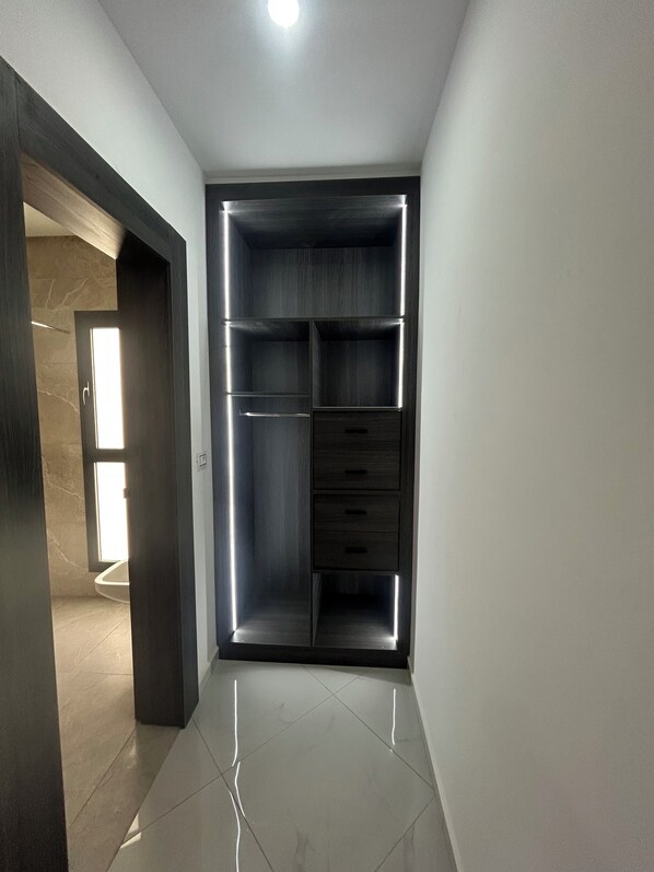 A modern interior with a built-in wardrobe featuring multiple drawers and shelves, a tiled floor, and a recessed ceiling light.