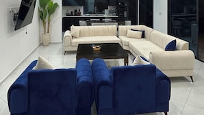 A modern living room with a sectional sofa, a coffee table, and a TV mounted on the wall. - VILLA BLANCA, a vacation villa with a pool and no neighbors in sight. Garage. 4 bedrooms. (Djerba Midun)