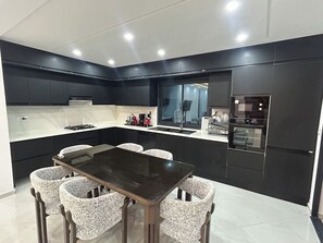 A modern kitchen with a central island, dark cabinetry, and a dining area with patterned chairs.