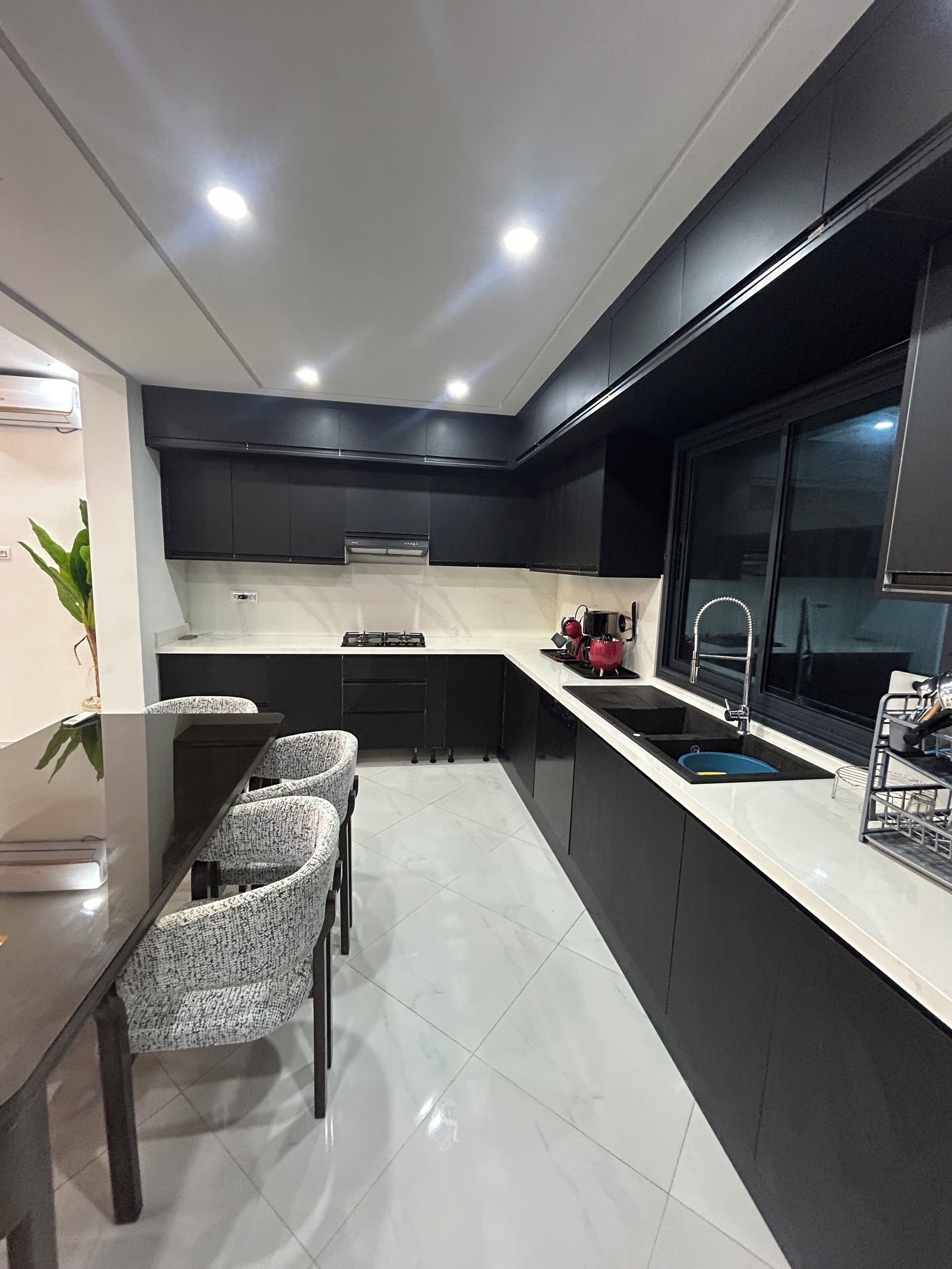 Une cuisine moderne dotée d’un îlot central, de meubles de couleur noire et d’un plan de travail blanc.