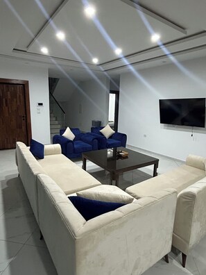A modern living room with a sectional sofa, a coffee table, and a flat-screen TV mounted on the wall.