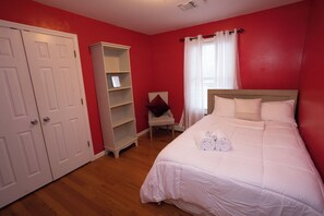 Ein Schlafzimmer mit einem Bett, weißen Vorhängen, einem weißen Kleiderschrank und Holzboden.