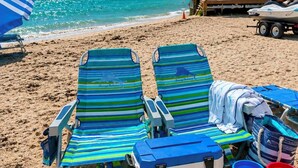 Une plage avec deux chaises longues à rayures, une glacière et des jouets de plage.