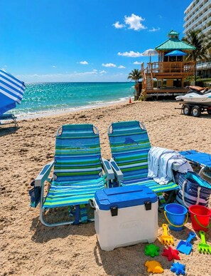 Ein Strand mit zwei gestreiften Liegestühlen, einer Kühlbox und Strandspielzeug.