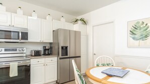 Une cuisine moderne avec des meubles blancs, des appareils en acier inoxydable, une machine à café et un distributeur d’eau.