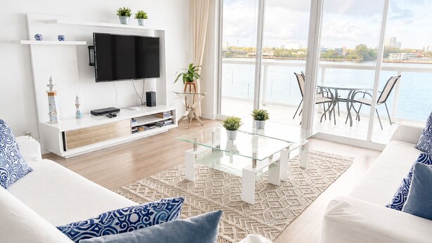 Un salon moderne doté d’un téléviseur à écran plat, de canapés blancs, d’une table basse en verre et offrant une vue sur une étendue d’eau.