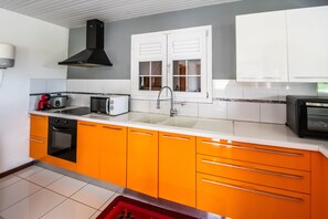 Eine Küche mit orangenen Schränken, einer schwarzen Dunstabzugshaube, einem Fenster mit weißen Fensterläden und einer Mikrowelle.