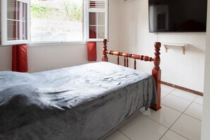 Ein Schlafzimmer mit Bett, Fenster und einem an der Wand befestigten Fernseher.