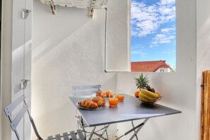 Un petit espace extérieur aménagé pour prendre les repas, avec une table dressée pour le petit-déjeuner, comprenant des croissants, des fruits et du jus d’orange.