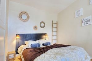 A bedroom with a bed, two wall-mounted lamps, a wooden ladder, and three wall decorations. - Le Cocon de Boucan Canot - À 300 m de la plage (La Possession)