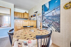 Een eetruimte met een ronde tafel, stoelen en een schilderij van een zeilschip aan de muur.
