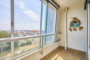 Een balkon met glazen hekwerk, uitzicht op een woonwijk en een decoratieve krans aan de muur.