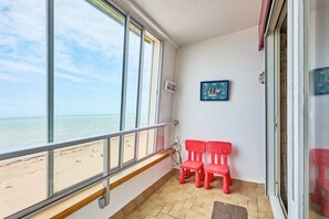 Ein Zimmer mit Blick auf den Strand, zwei rote Stühle, ein gerahmtes Bild und ein Fenster mit Metallgitter.