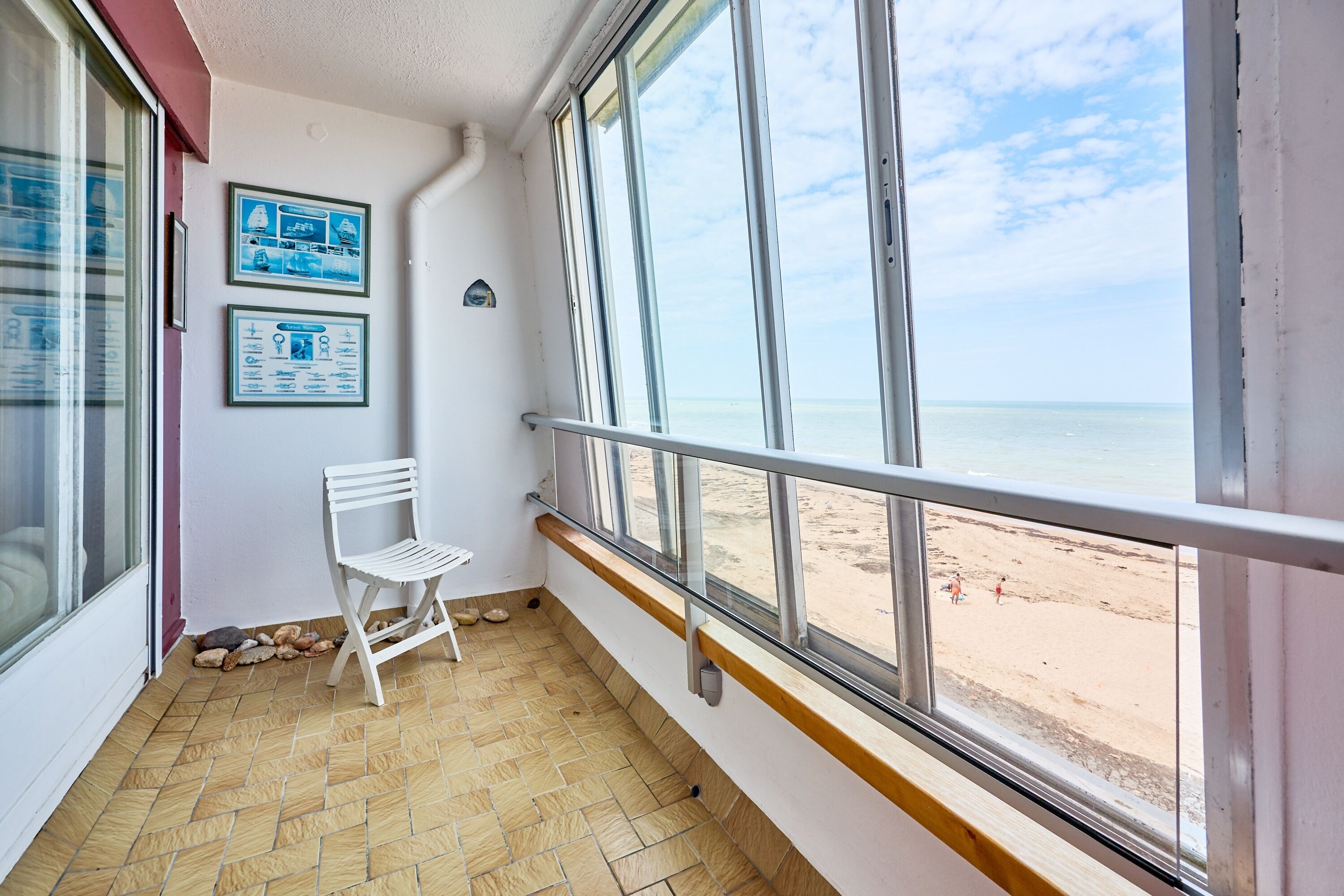 Un balcon avec une chaise blanche, un sol carrelé et une vue sur la plage.